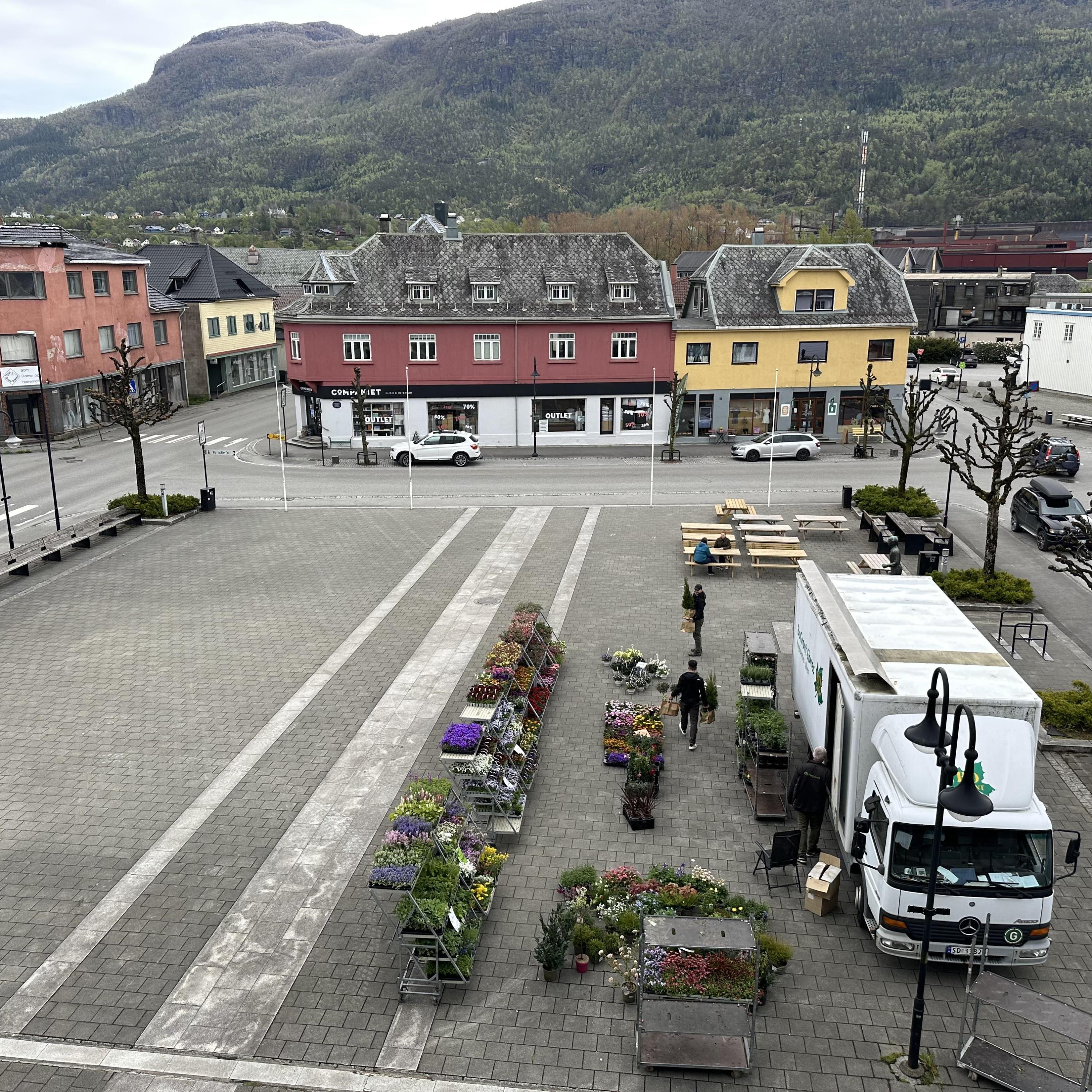 Liten lastebil med mye blomster stilt opp ved siden av seg på torget